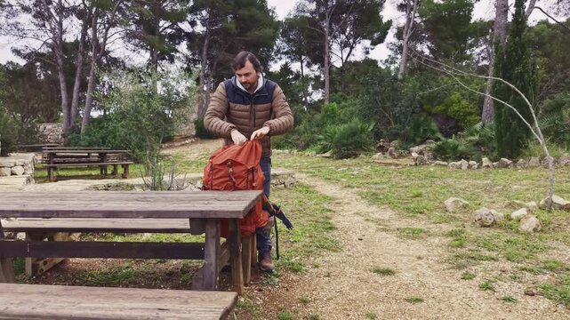 Man resting at picnic table drinking from mug during hiking trip