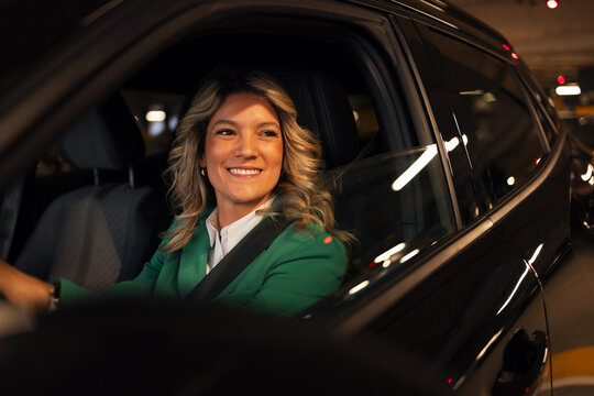 Smiling businesswoman driving car in urban parking garage