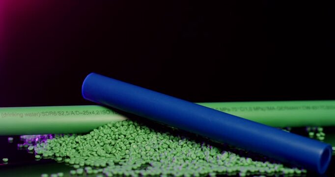 Close up of blue and green industrial plastic pipes resting on a pile of polymer granules against a dark background