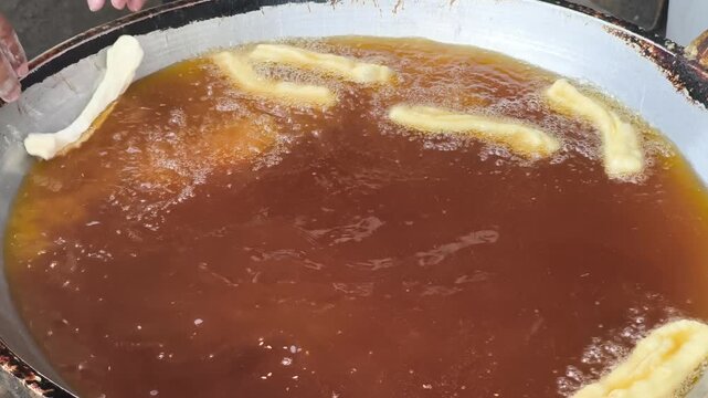 Close-up of cakwe being fried in a sizzling hot brown oil mixture in a pan, likely a traditional Indonesian culinary process.