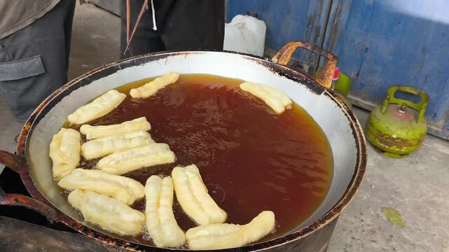 Traditional Indonesian cakwe being deep-fried in a large pan of hot oil on a street food stall in Indonesia.