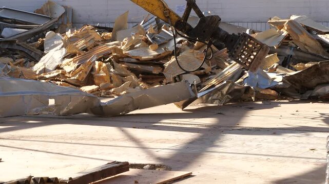 yellow excavator's hydraulic sorting grapple working at a
demolition site. The mechanical attachment moves through a pile of light
colored stone debris and crumpled metal cladding. A red construction 