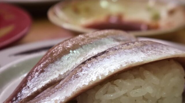 Fresh whole sardine or iwashi nigiri sushi two pieces on ceramic plate with shiny silver skin, Japanese restaurant