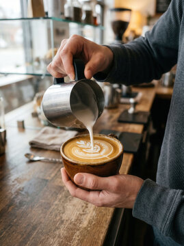 Barista pouring steamed milk into a coffee cup to create latte art in a cafe