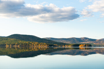 Fototapeta premium Beautiful lake at sunset. Mountains, trees and sky are reflected in the calm water surface.