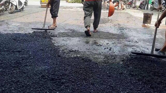 Manual Road Paving and Asphalting Process        Workers manually leveling hot asphalt mix using wooden rakes on a road surface during a local construction project.