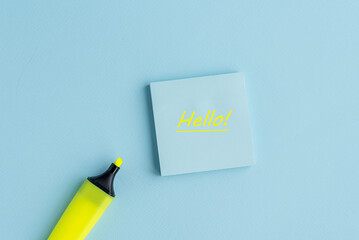 A blue sticky note with the word 'Hello ' written in bright yellow. A yellow highlighter is placed beside it on a light blue background. © Татьяна Зернова
