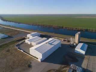 Obraz premium An aerial view showcases a complex of white industrial buildings including grain silos alongside a winding river and farmland high quality professional detailed