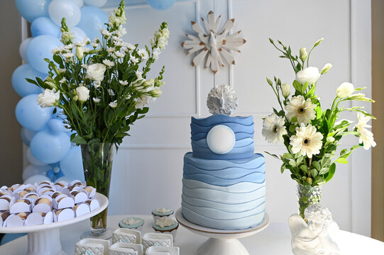 elegant religious celebration cake table with blue and white decor, modern baptism or first communion event setup with floral arrangements and angel souvenirs, spiritual ceremony decoration