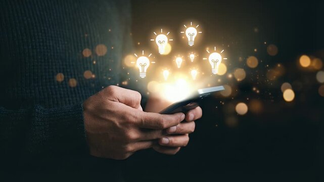 Close-up of hands holding a black smartphone with glowing white lightbulb icons floating above the screen, dark background with warm bokeh particles, cinematic technology stock footage style for creat