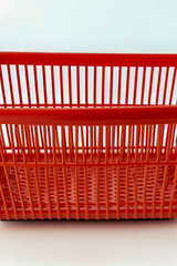 Fototapeta premium A small, bright red plastic basket sits on a clean white surface. vertical frame