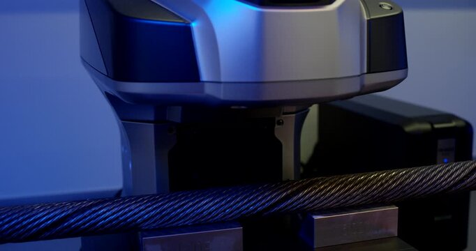 Close up of industrial measurement equipment scanning a steel wire rope with laser light in a laboratory setting