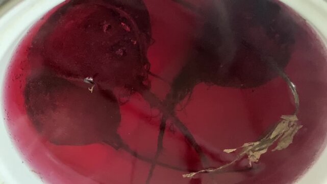 Whole organic beetroots cooking in vibrant red boiling water inside a kitchen pot viewed from above.