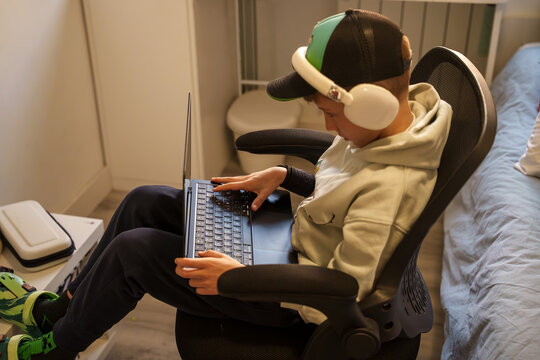 Ni&ntilde;o concentrado usando un ordenador port&aacute;til con auriculares en su habitaci&oacute;n.