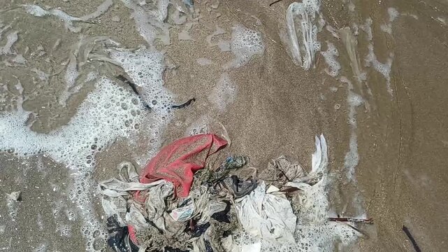 Ocean pollution from plastic waste washes ashore with waves and foam