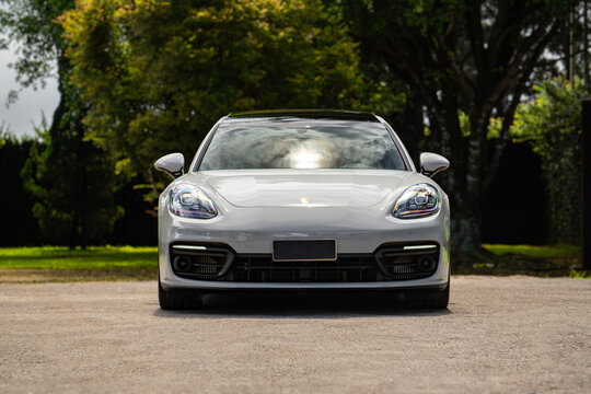 Grey Porsche Panamera 4S straight front view near green nature, luxury sedan facing forward on driveway by trees