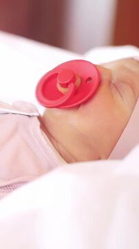 A baby rests peacefully with a pink pacifier in their mouth. The baby is lying on a soft, white surface, exuding calmness and tranquility throughout the scene.