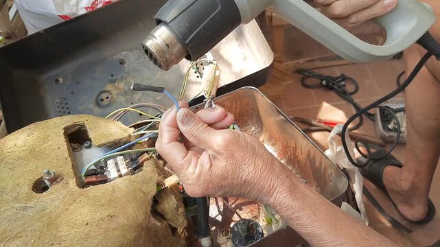 Close up of technician repairing an industrial steam iron boiler, using a heat gun on internal wiring and components protected by thermal insulation material.