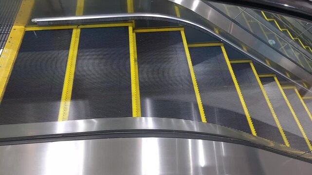 An empty escalator moving up in a modern building, providing a moving staircase that carries people between different floors with sleek metal and glass design.
