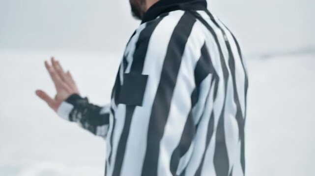 Hockey referee in striped uniform gesturing on ice rink during game. Official sports environment, rules enforcement, competition control and professional gameplay atmosphere.