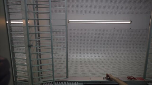 Male technician's hand is pressing a button to turn on a long fluorescent tube light attached to a perforated wall in a modern workshop