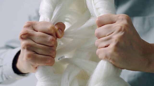 Gripping shirt-cuffed hands pulling braided fiber open in studio, probing fibers to check structure