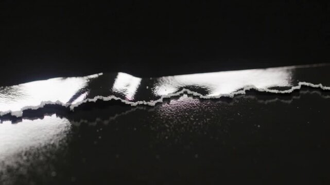 Tearing glossy black film exposing white substrate under studio light, flap forming, flakes lifting