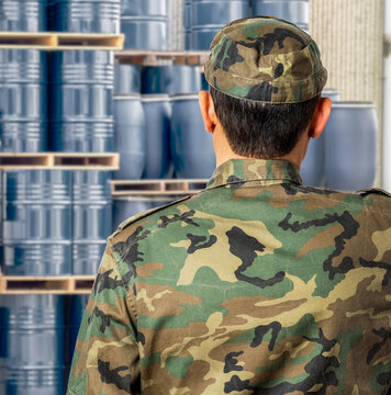 Rear view of a security guard watching over a warehouse of oil barrels in war