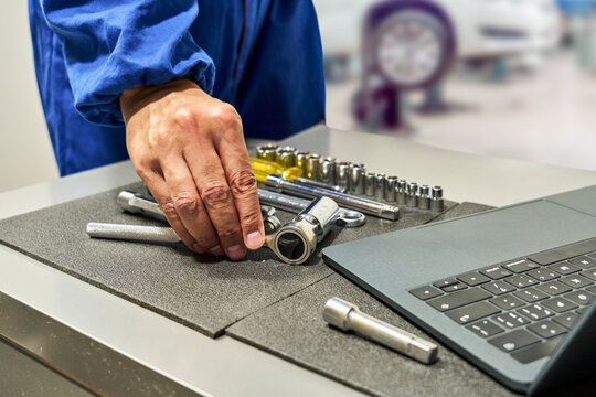 Repairman's hands grabbing a tool from his toolbox and consulting his laptop for information about the car.