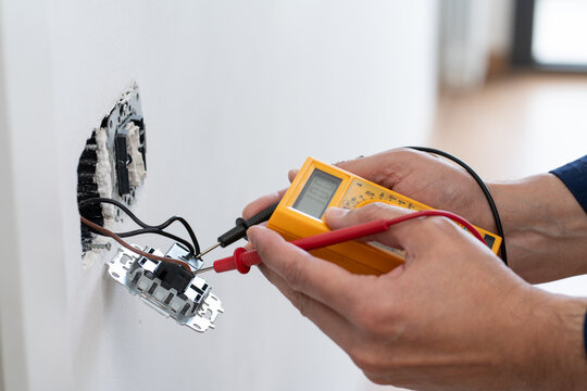 Close-up on an hands of electrician fixing an electrical outlet and measuring the voltage at a house - home improvement concepts