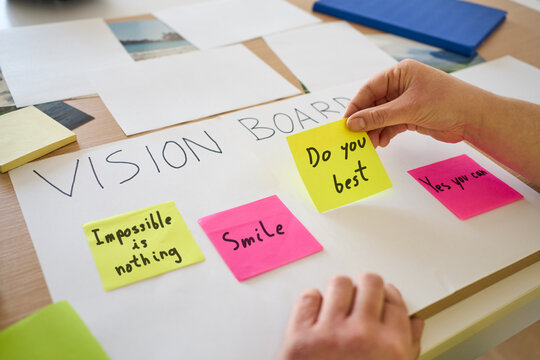 Woman writing on vision board in home for planning goals, aspirations and manifestation. Poster, pictures and sticky notes for inspiration, progress tracking and personal development