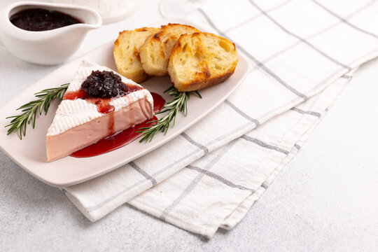 Soft pink camembert cheese with rose flavor served with toast and rosemary, topped with dripping rose jam on a light background with a copy space.