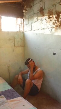 A criminal is crying, showing remorse and frustration, while sitting next to a bed in his cell inside a prison in Neiva, Huila, Colombia. Concept of sadness and psychological trauma