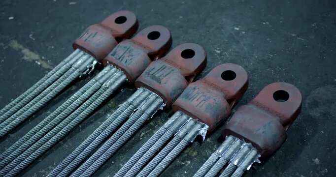 Row of heavy duty steel wire rope cables with metal terminal sockets in an industrial workshop