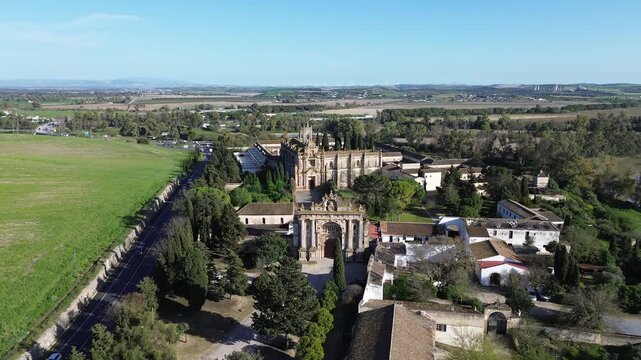 Aerial drone shot moving backwards and ascending in 4K resolution revealing a wide panoramic view of La Cartuja Monastery in Jerez de la Frontera with surrounding farmlands and a highway with cars