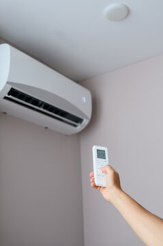 Male hand holding remote control and pointing at air conditioner on wall, smart home climate control system, cooling and heating equipment, domestic comfort and energy saving concept, HVAC