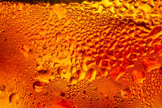 A macro shot of a cola drink showing cold condensation droplets on an amber-colored glass surface,Close-up macro photography of fresh water droplets and condensation on a chilled amber or orange.