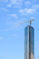 Fototapeta premium Modern glass skyscraper under construction in Batumi Georgia. High-rise building with tower crane against sky. Real estate development, urban architecture, modern engineering, property investment