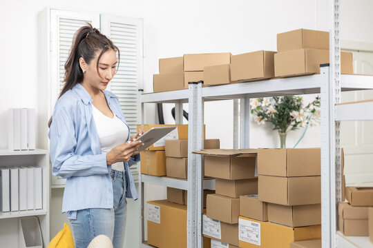 Inventory, stock, storage, warehouse, tracking, small business owner reviews order using tablet near stacked parcels, checking item availability and shelf arrangement in home warehouse for control.