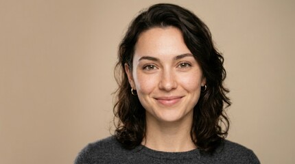 Fototapeta premium Portrait of a smiling young woman with dark, wavy hair and warm brown eyes, looking confidently at the camera on a plain background.