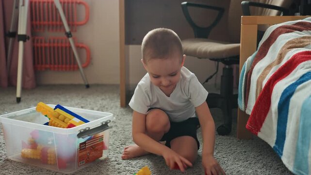 Son sorting and stacking blocks quietly, toddler selects pieces from clear bin and assembles colorful structures on carpet, patient focus and careful hands create creative learning moment in sunlit
