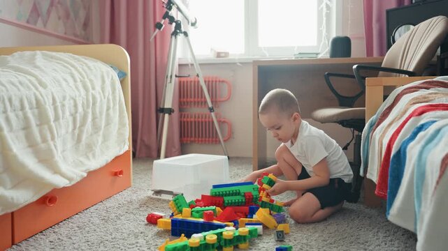 Boy concentrates while building colorful structures. Young child carefully constructs vibrant shapes on bedroom rug. Youthful builder focuses intently as he creates lively block formations on carpet