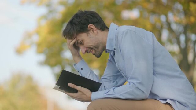 Close up of a man reading a book with intense focus in a sunny park.