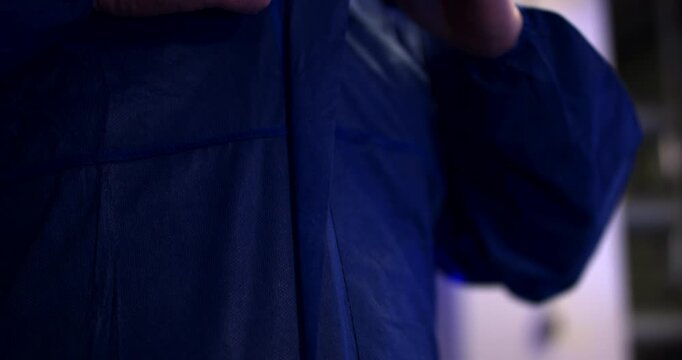 Close up of a worker zipping up a blue protective work coverall in an industrial environment