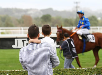 Público con padre y su hijo en brazos en hipódromo viendo caballo de carreras  © Diego