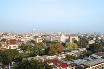 Fototapeta premium A high-angle, panoramic shot overlooking a bustling urban landscape in Bangkok, Thailand. The scene highlights the contrast between the lush green trees and traditional temple architecture.