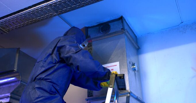 Technician in blue protective suit and safety gloves inspecting an industrial ventilation system
