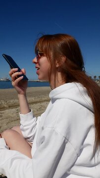 Young woman dictating text with AI voice chat on smartphone by the sea.
