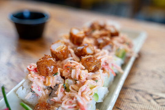 Gourmet sushi roll with creamy spicy crab mix, avocado, and crispy fried shrimp pieces, drizzled with sauce