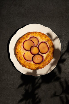 Baked cheesecake with fresh fruit slices on top served on white plate with dramatic light and shadows